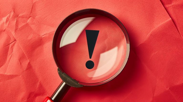 Be careful! Magnifying glass on red paper with exclamation mark for important alert, danger, or hazard